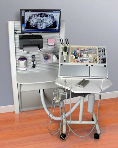 Ergonomic Headwall cabinetry with built-in monitor, upper and lower storage, and sink in a modern dental treatment room.